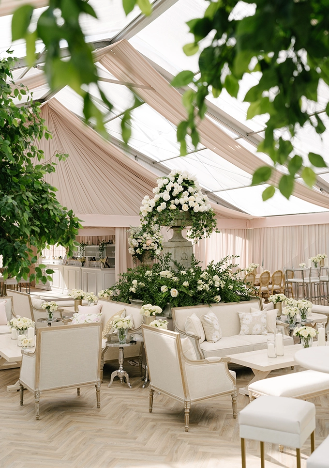 Full decorated high-peak tent rental with white fabric sofas and beautiful white floral arrangements