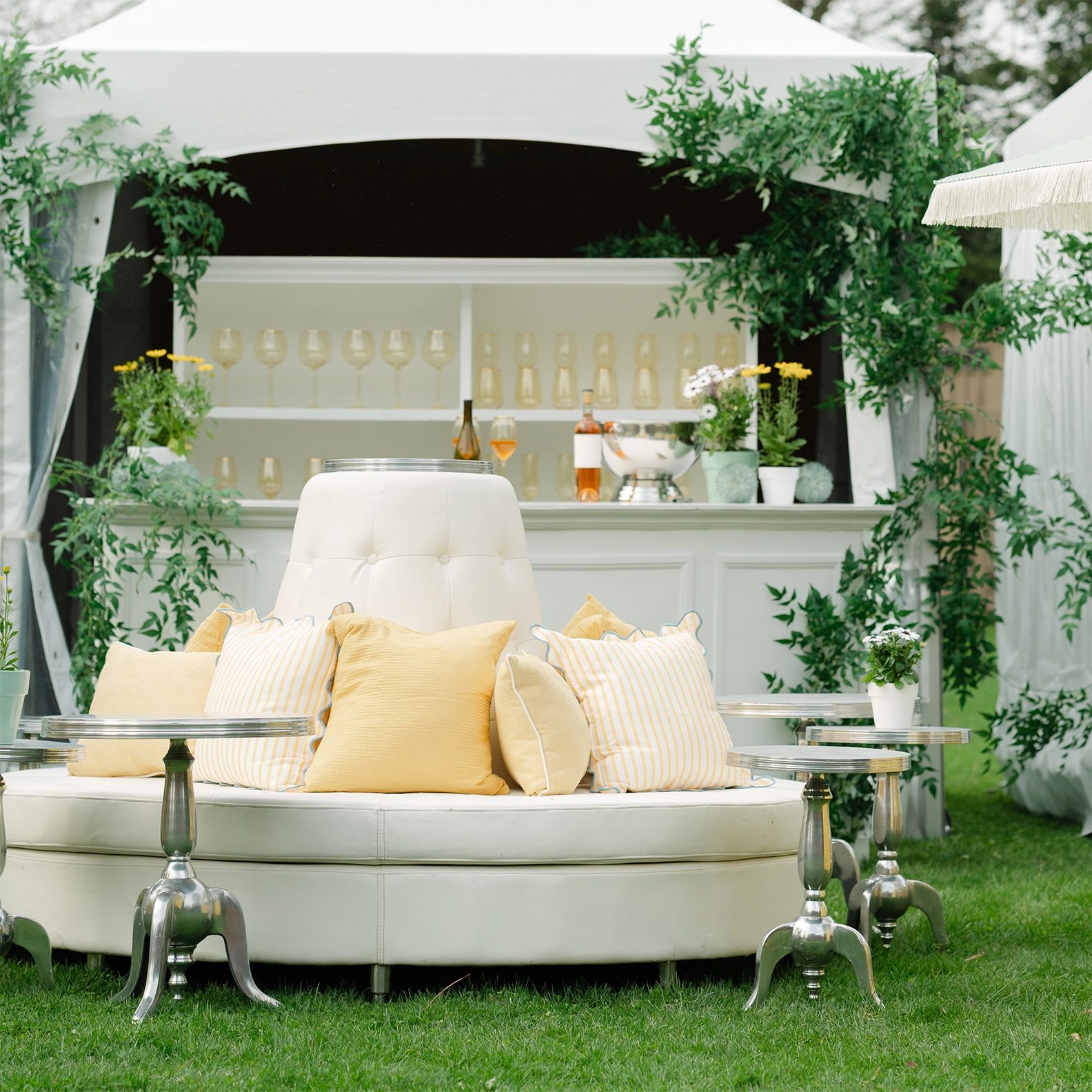 White circular lounge sofa with light yellow throw pillows in front of a wine bar located in a High-Peak tent
