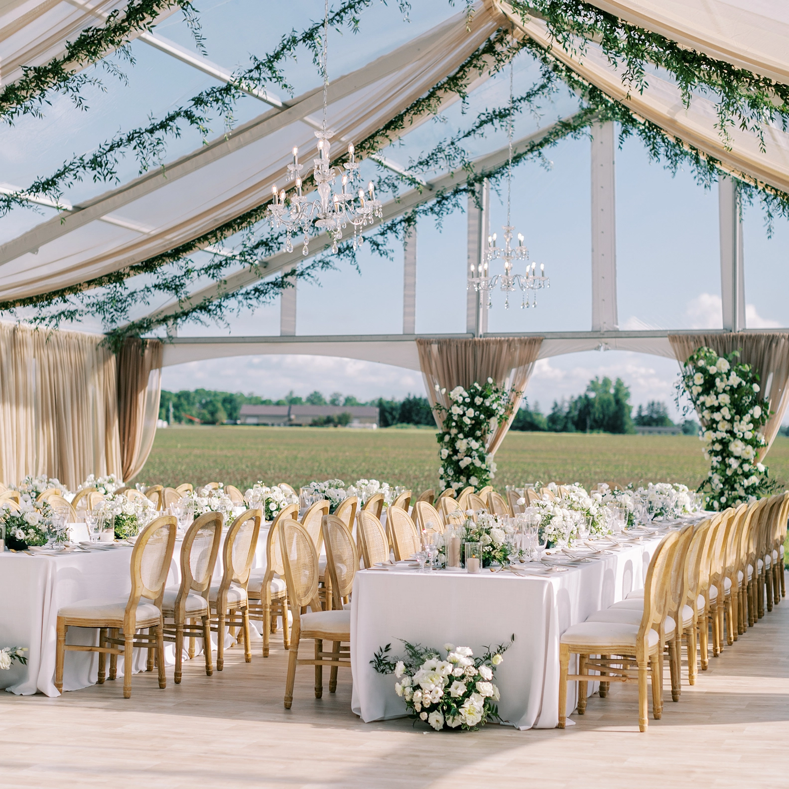 Legacy Tent from Special Event Rentals setup outdoors with linen treatment and greenery hanging from the vaulted ceiling