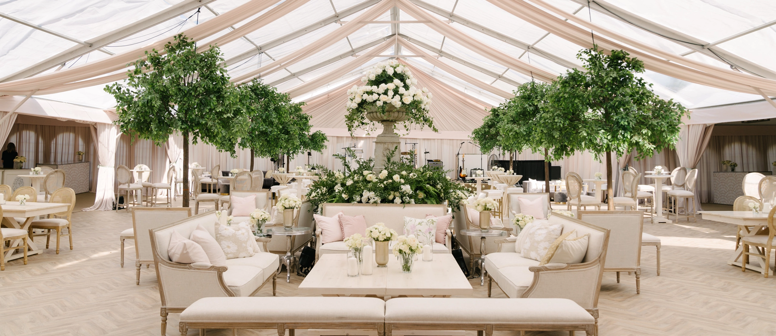 Beautiful outdoor tented event with white fabric lounge furniture and soft white and pink accent pillows and florals