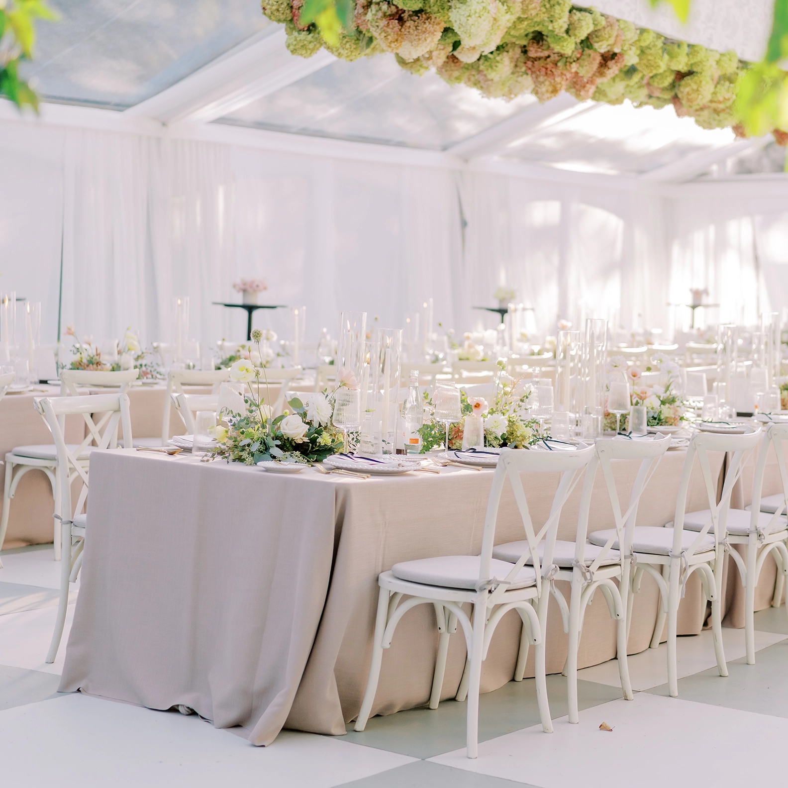 Dinner event with white wooden chairs and soft neutral table linens, with hydrangeas suspended from the ceiling