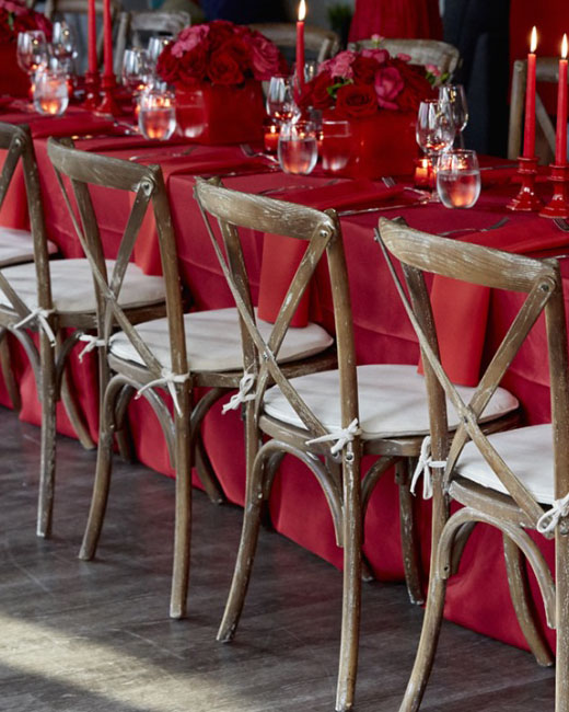 A photo of a table with wooden chairs and red table linens